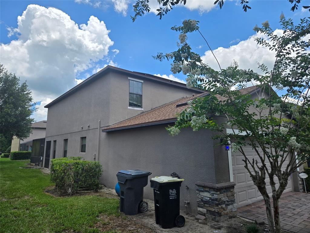 The exterior of a two-story stucco home features a garage, driveway, and two trash bins — 1120 CYPRESS POINTE BOULEVARD, DAVENPORT, FL