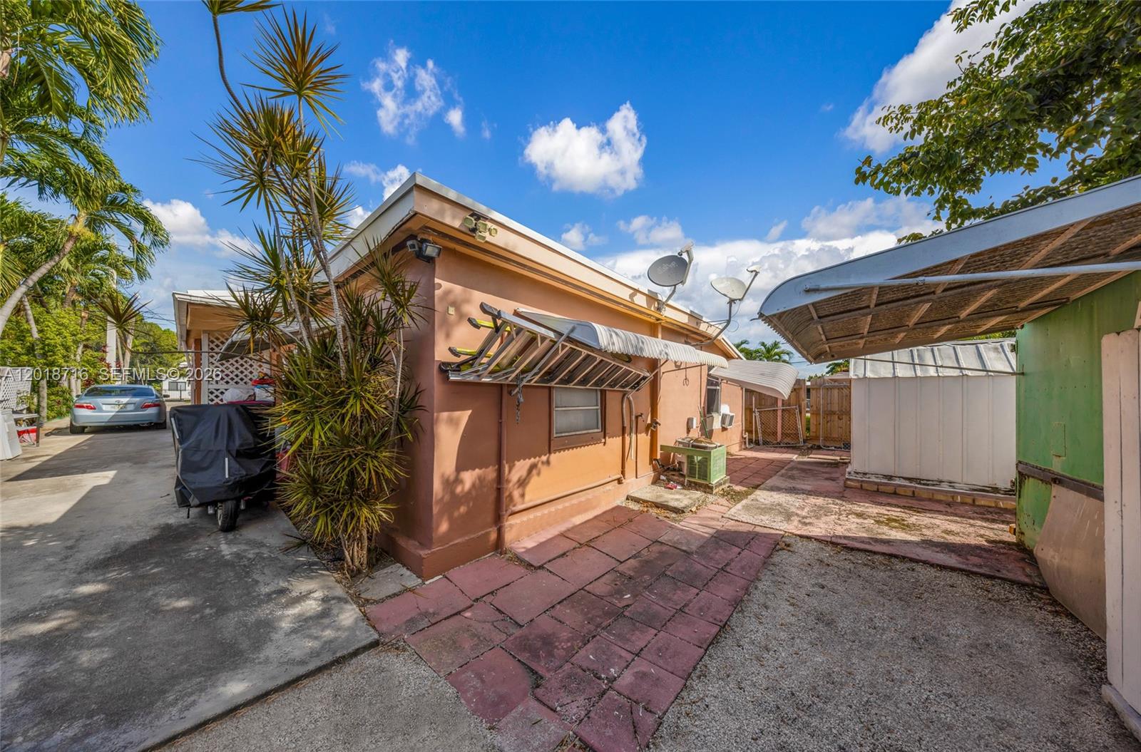 The exterior of a tan house features a paved patio, a ladder, and satellite dishes — 3126 NW 28th St, Miami FL 33142, MIAMI, FL