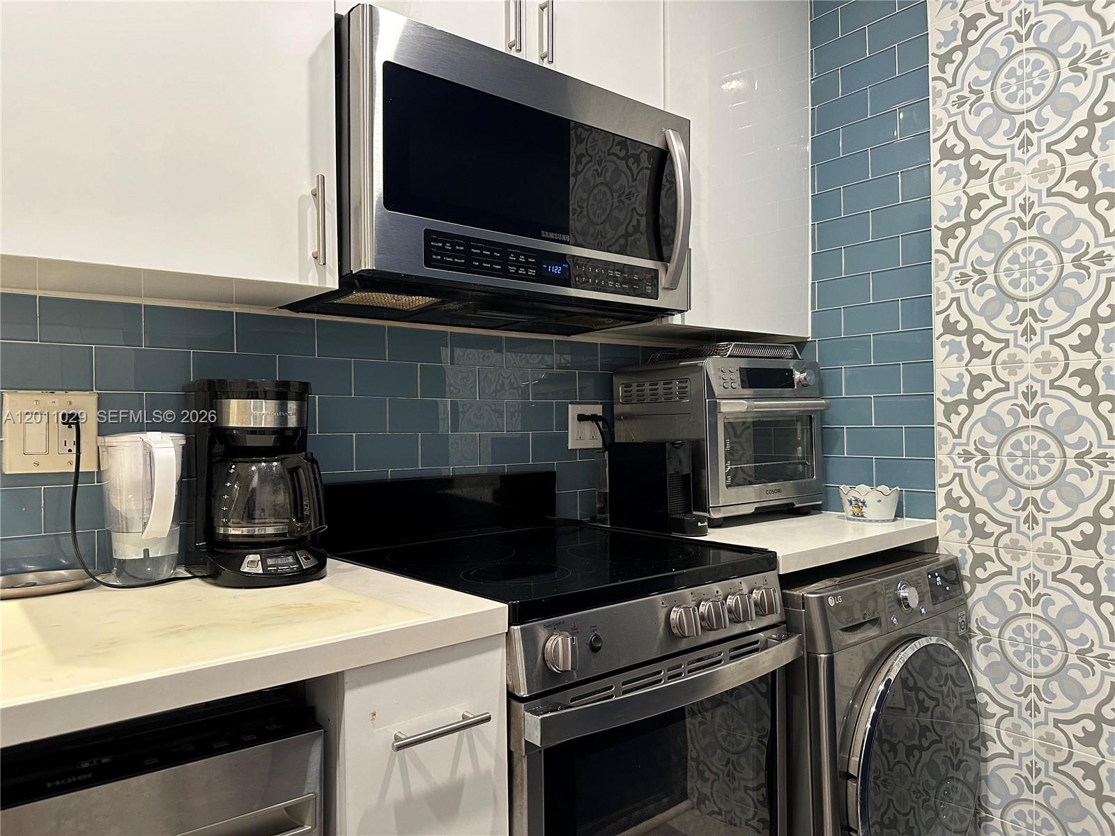 A kitchen features white cabinets, blue subway tile backsplash, stainless steel appliances, and patterned wall tiles — 1130 11th St # 4E, Miami Beach FL 33139, MIAMI BEACH, FL