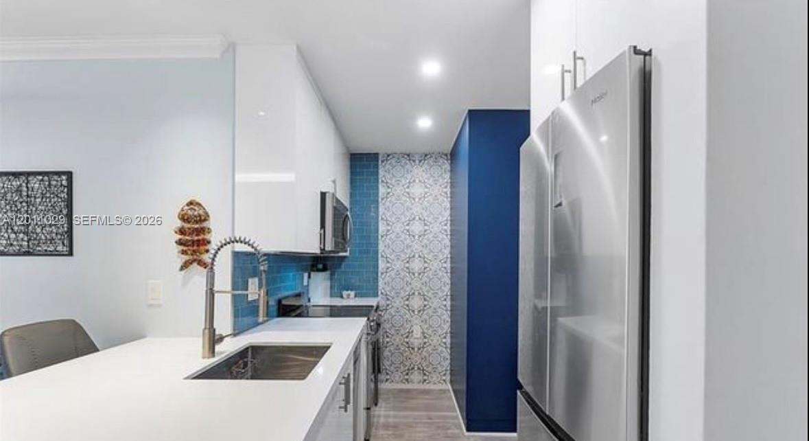A modern kitchen features white cabinets, blue tile backsplashes, a stainless steel refrigerator, and sink — 1130 11th St # 4E, Miami Beach FL 33139, MIAMI BEACH, FL