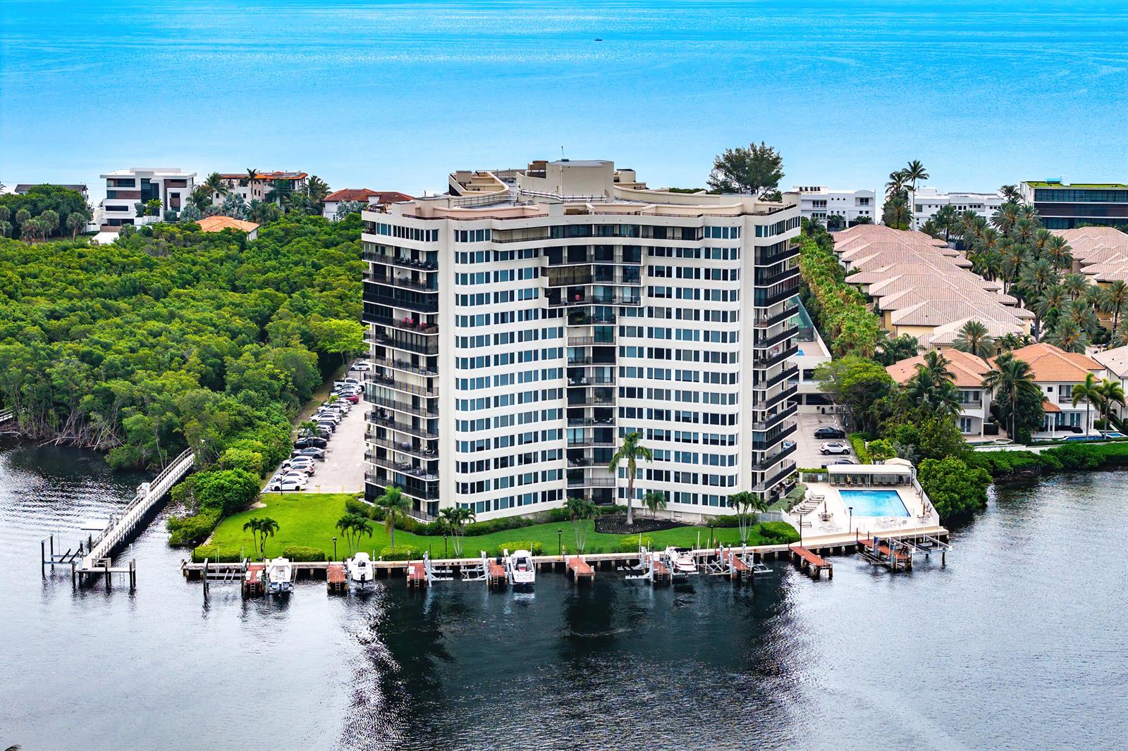 An aerial view shows a tall residential building surrounded by water, lush trees, and boat docks — 3912 S Ocean Boulevard # 612, Highland Beach FL 33487, HIGHLAND BEACH, FL