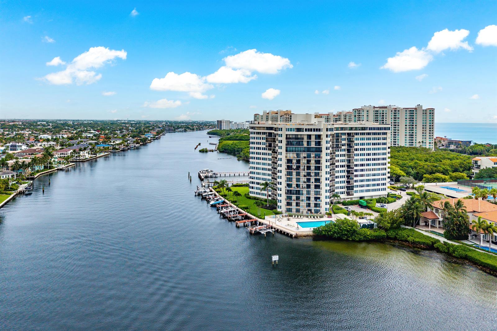An aerial view shows a tall apartment building beside a canal with boat docks — 3912 S Ocean Boulevard # 612, Highland Beach FL 33487, HIGHLAND BEACH, FL