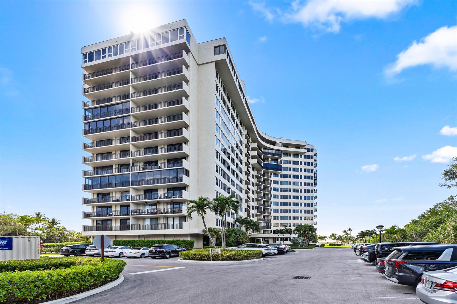 A tall, multi-story residential building with balconies stands above a parking lot with cars — 3912 S Ocean Boulevard # 612, Highland Beach FL 33487, HIGHLAND BEACH, FL