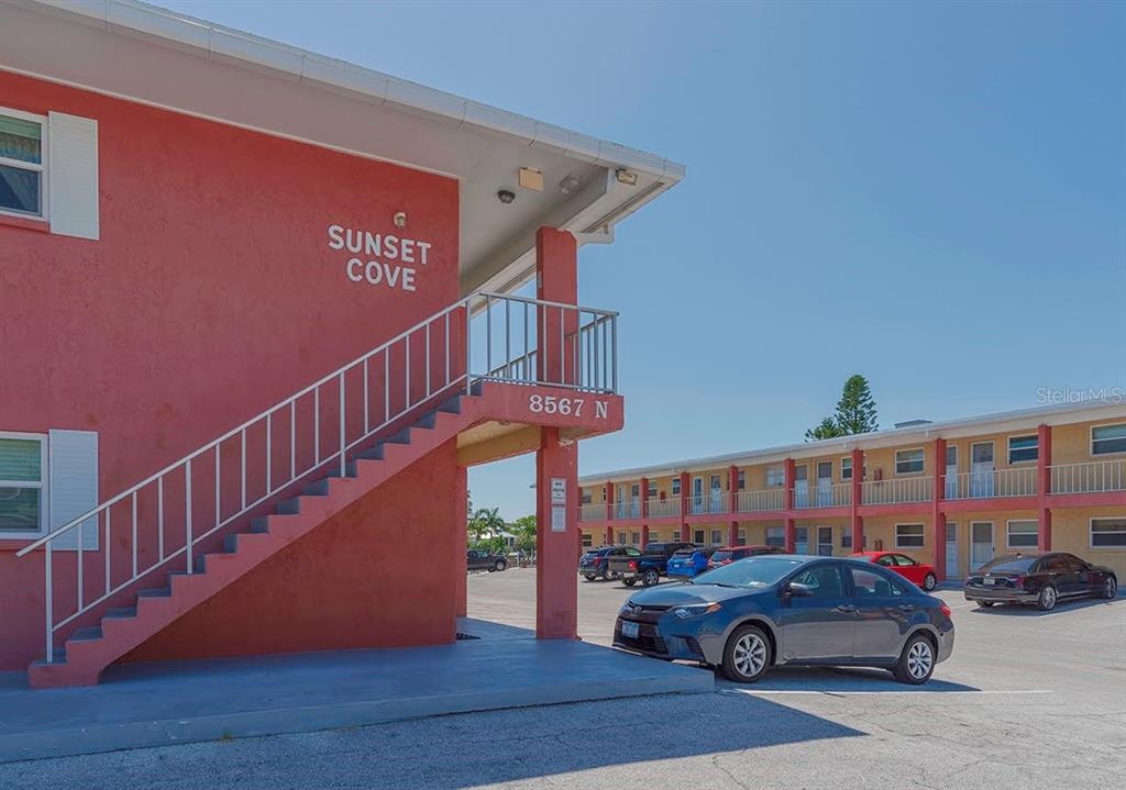 A red two-story apartment building with exterior stairs and a parking lot in front — 8567 W GULF BOULEVARD UNIT 3N, ST PETERSBURG, FL