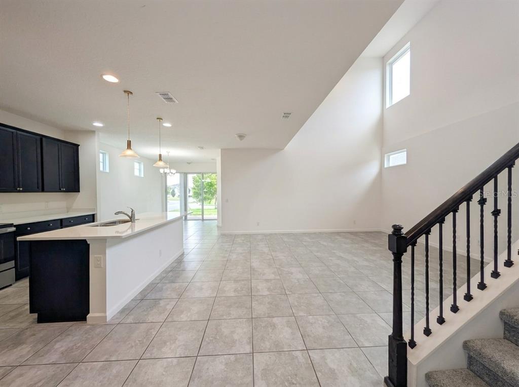 A kitchen with dark cabinets and a white island opens to a tall living area — 2275 ABILIA ALLEY, APOPKA, FL