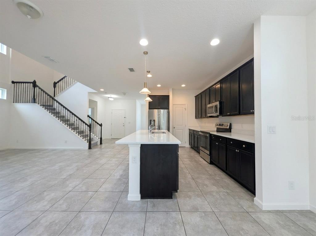 A kitchen with dark cabinets, white countertops, and an island overlooks a staircase — 2275 ABILIA ALLEY, APOPKA, FL