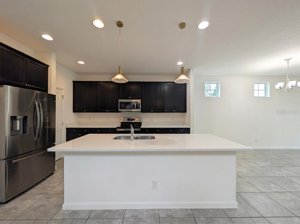 A kitchen features dark cabinets, stainless steel appliances, a white island, and tile flooring — 2275 ABILIA ALLEY, APOPKA, FL