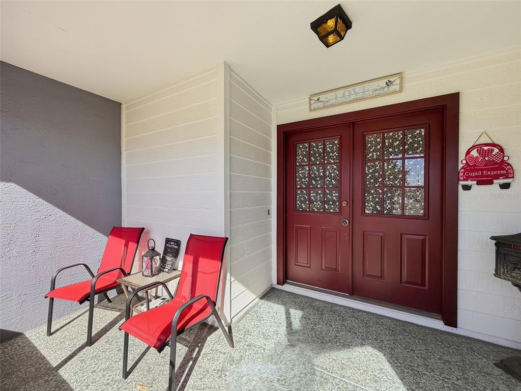 A covered front porch features two red chairs, a small table, and double red doors — 10654 FALLEN LEAF LANE, PORT RICHEY, FL