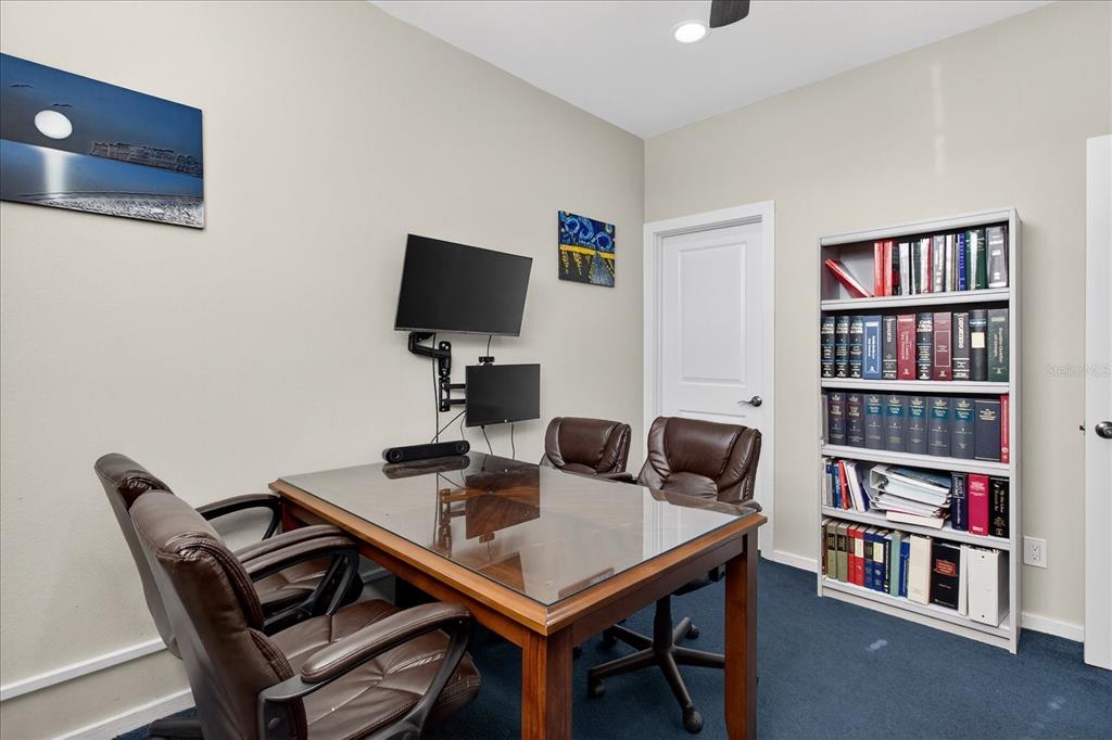 A home office features a glass-topped desk, leather chairs, a wall-mounted television, and a bookshelf — 10225 ULMERTON ROAD UNIT 12B, LARGO, FL