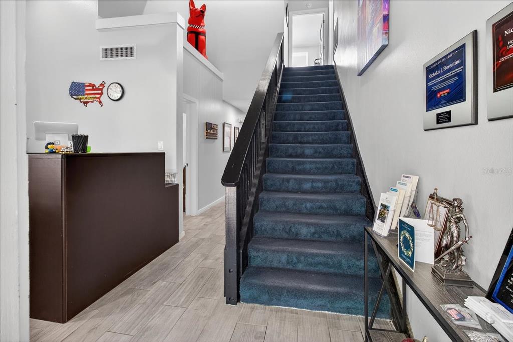 A reception area features a dark desk, blue carpeted stairs, and light wood-look tile flooring — 10225 ULMERTON ROAD UNIT 12B, LARGO, FL