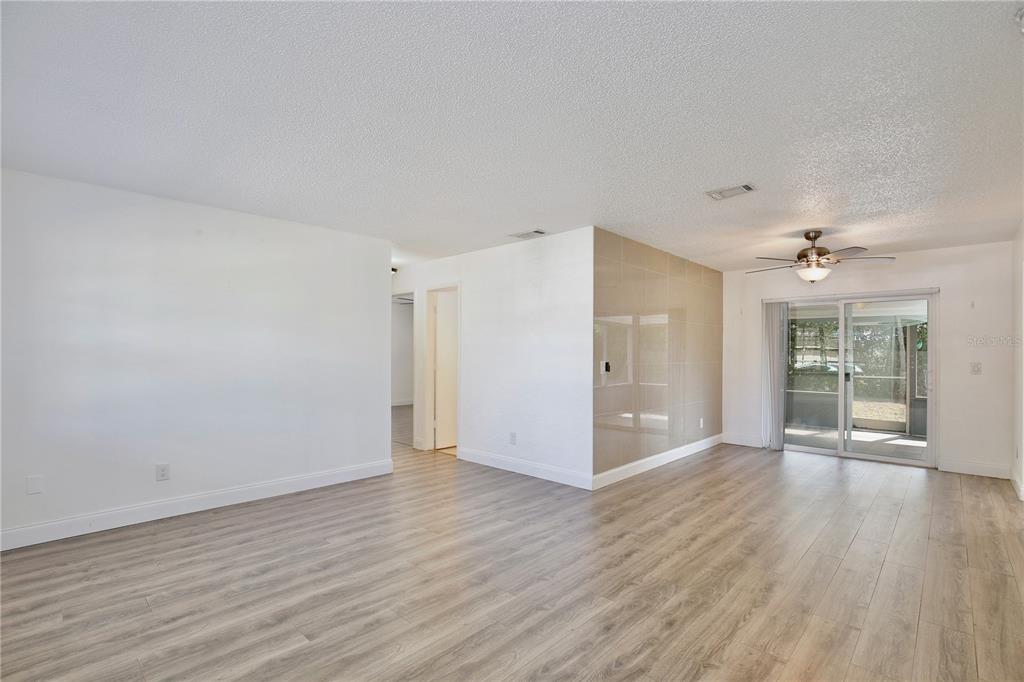An empty living room with light wood-look flooring, white walls, and a sliding glass door — 1847 FAYETTEVILLE AVE, DELTONA, FL