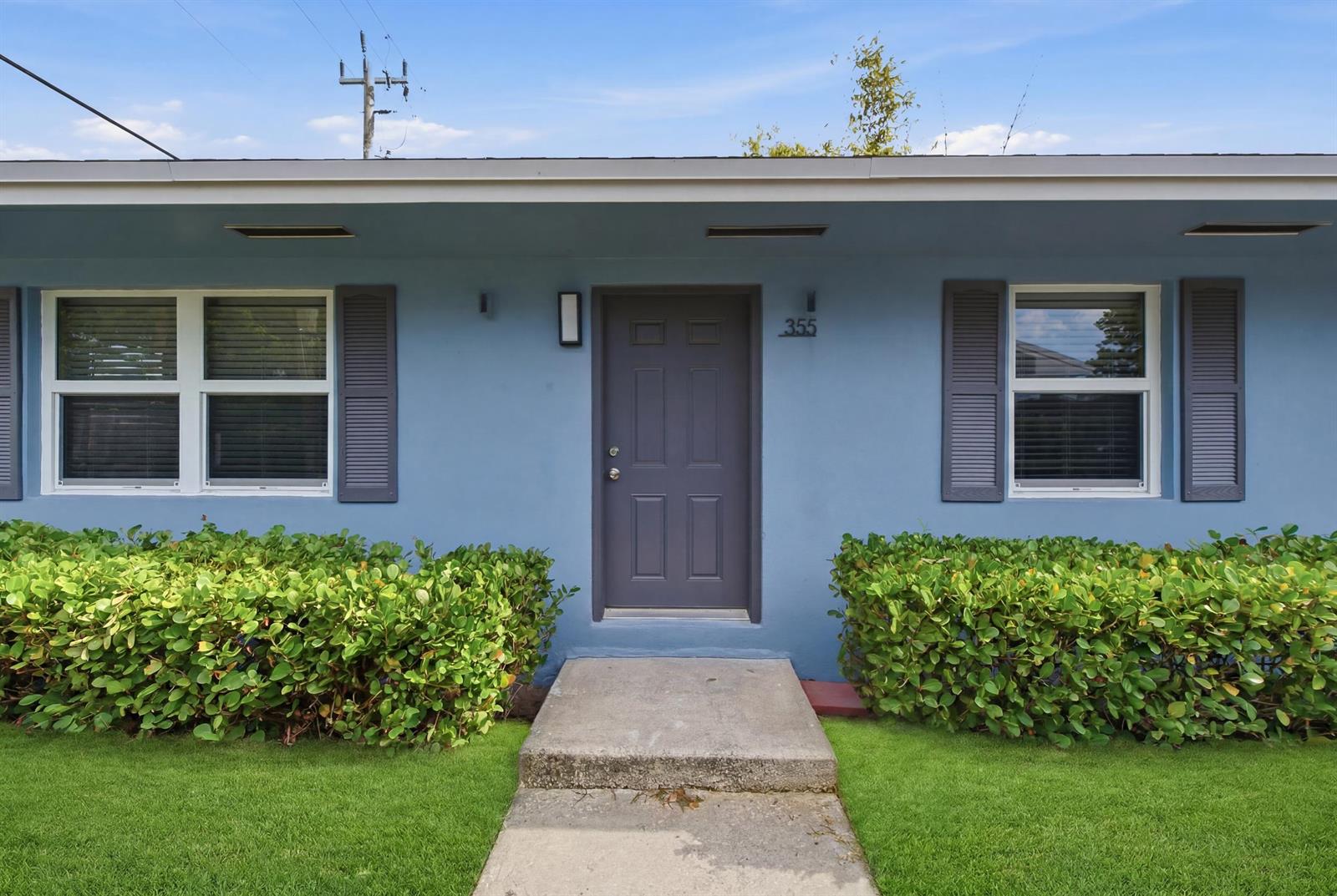 A blue house exterior features a gray front door, shutters, and green landscaping — 355 Wickline Boulevard, Lantana FL 33462, LANTANA, FL