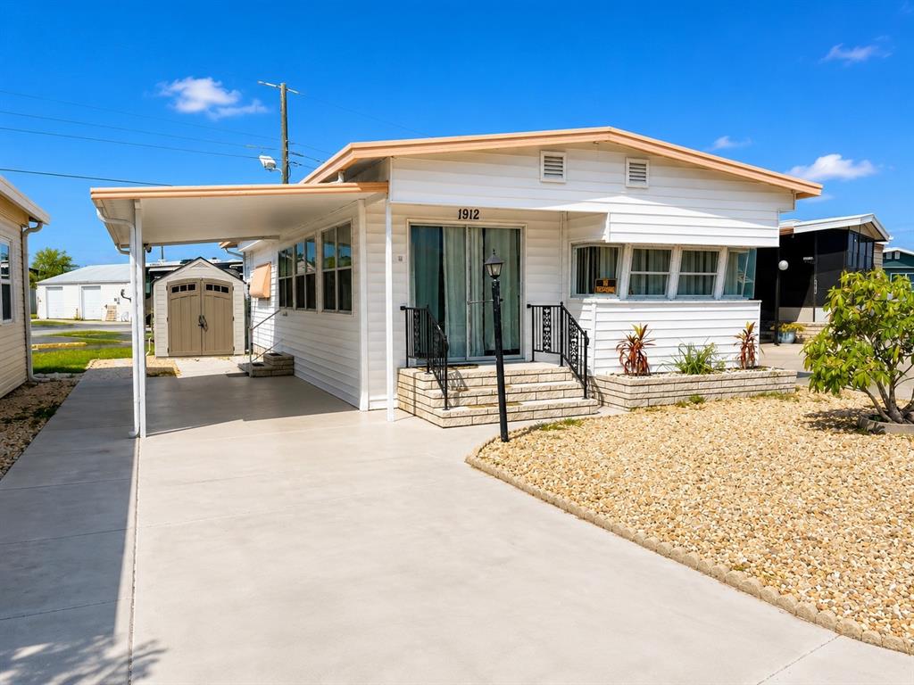 A white mobile home with a carport, concrete driveway, and a gravel front yard — 1912 IOWA AVENUE, BRADENTON, FL