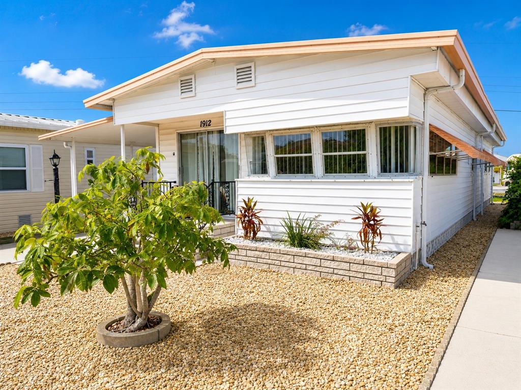 A white mobile home with a gravel yard, a small tree, and a brick planter — 1912 IOWA AVENUE, BRADENTON, FL