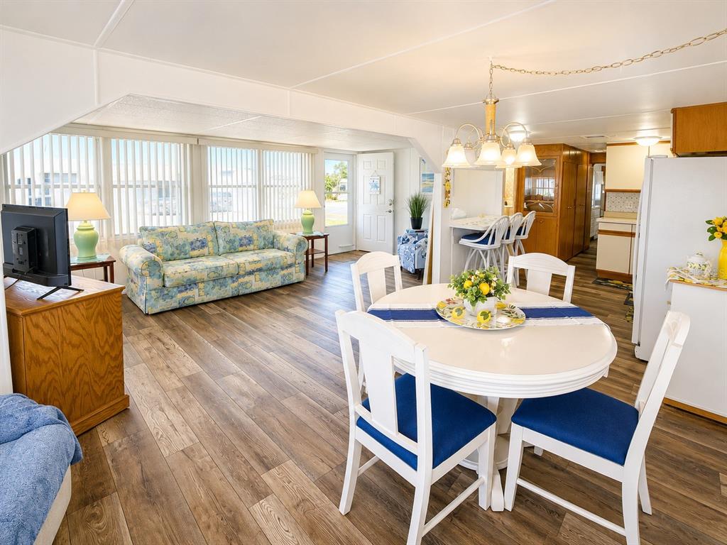 An open-concept living and dining area features wood-look flooring, a floral sofa, and white furniture — 1912 IOWA AVENUE, BRADENTON, FL