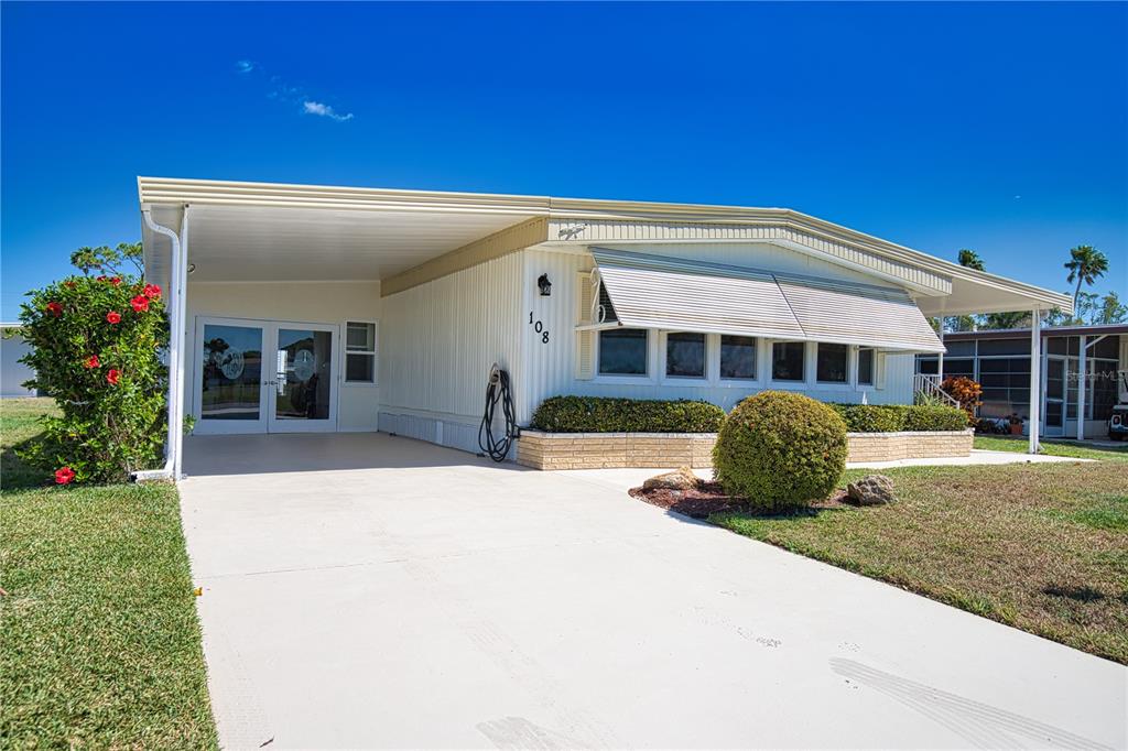 A single-story manufactured home with a white exterior, a concrete driveway, and a carport — 108 LA PALOMA, NORTH PORT, FL