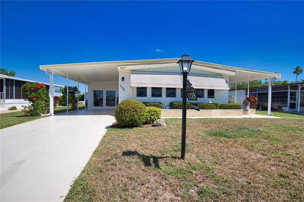 A single-story manufactured home with a carport, white siding, and a front lawn — 108 LA PALOMA, NORTH PORT, FL