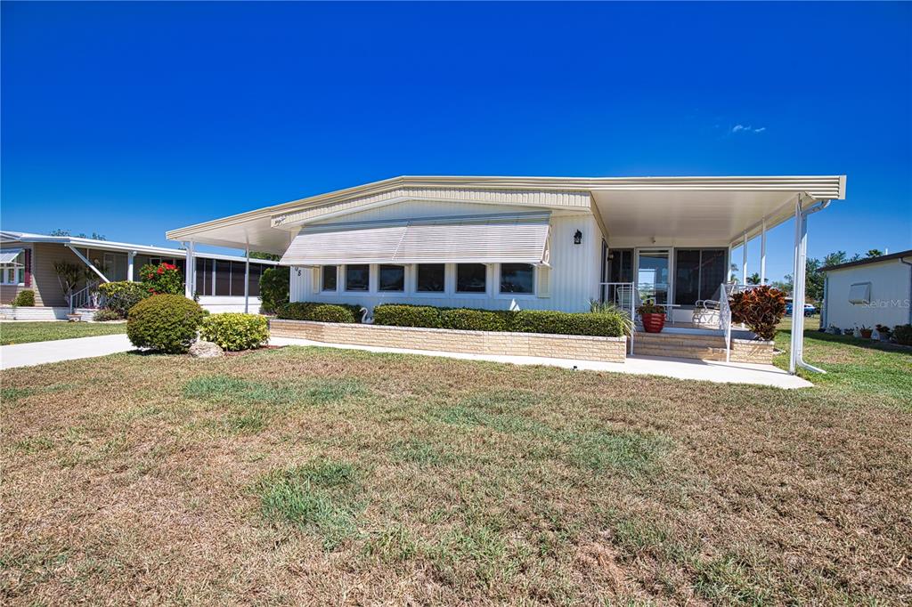 A single-story manufactured home with a covered carport and a front porch under a clear sky — 108 LA PALOMA, NORTH PORT, FL