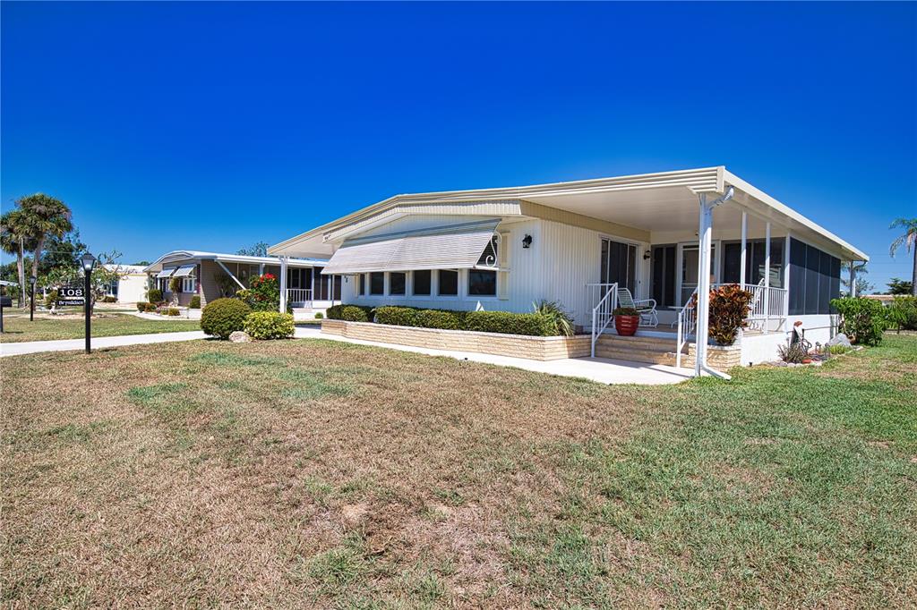 A single-story manufactured home with a covered porch and a large grassy front yard — 108 LA PALOMA, NORTH PORT, FL
