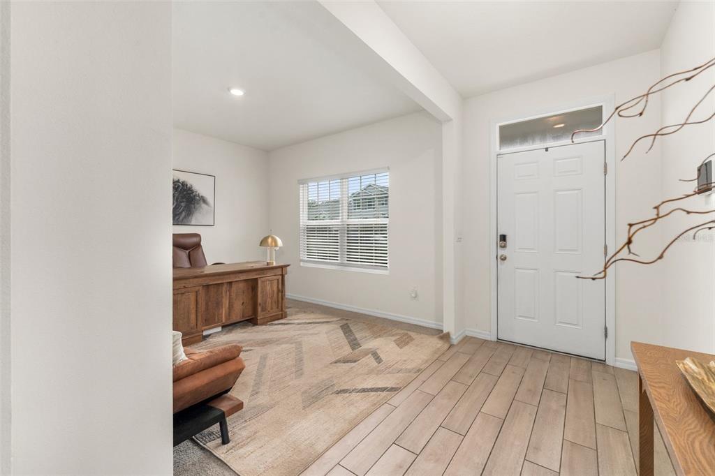 An entryway with wood-look tile flooring leads into a carpeted home office with a desk — 1443 NW 140TH WAY, NEWBERRY, FL