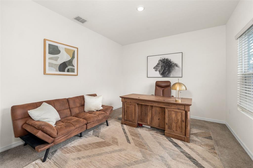 A home office features a brown sofa, a wooden desk, and a lion wall print — 1443 NW 140TH WAY, NEWBERRY, FL