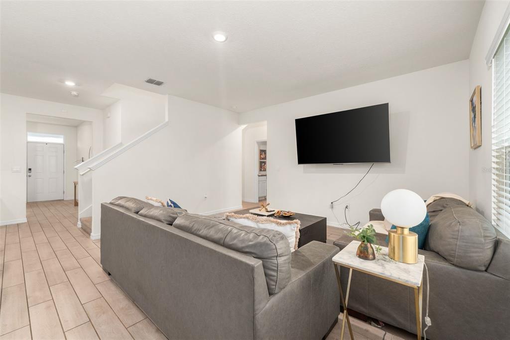 A living room features gray sofas, a wall-mounted television, and light-colored tile flooring — 1443 NW 140TH WAY, NEWBERRY, FL