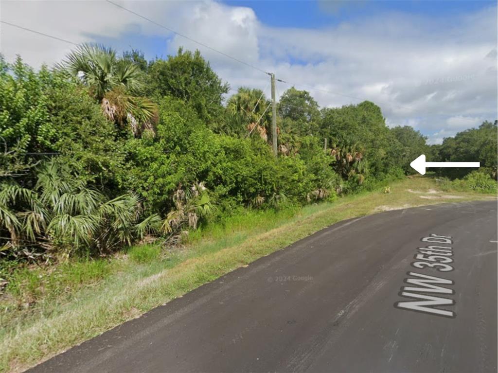 A paved road curves past a dense, wooded lot with a utility pole and vegetation — 3093 NW 35TH DRIVE, OKEECHOBEE, FL