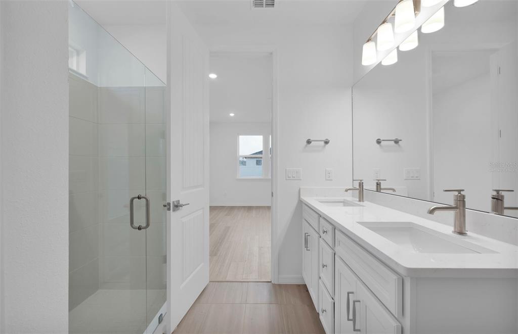 A modern bathroom features a double vanity, a glass-enclosed shower, and light-colored tile flooring — 83 LAKE MANATEE DRIVE, PALM COAST, FL