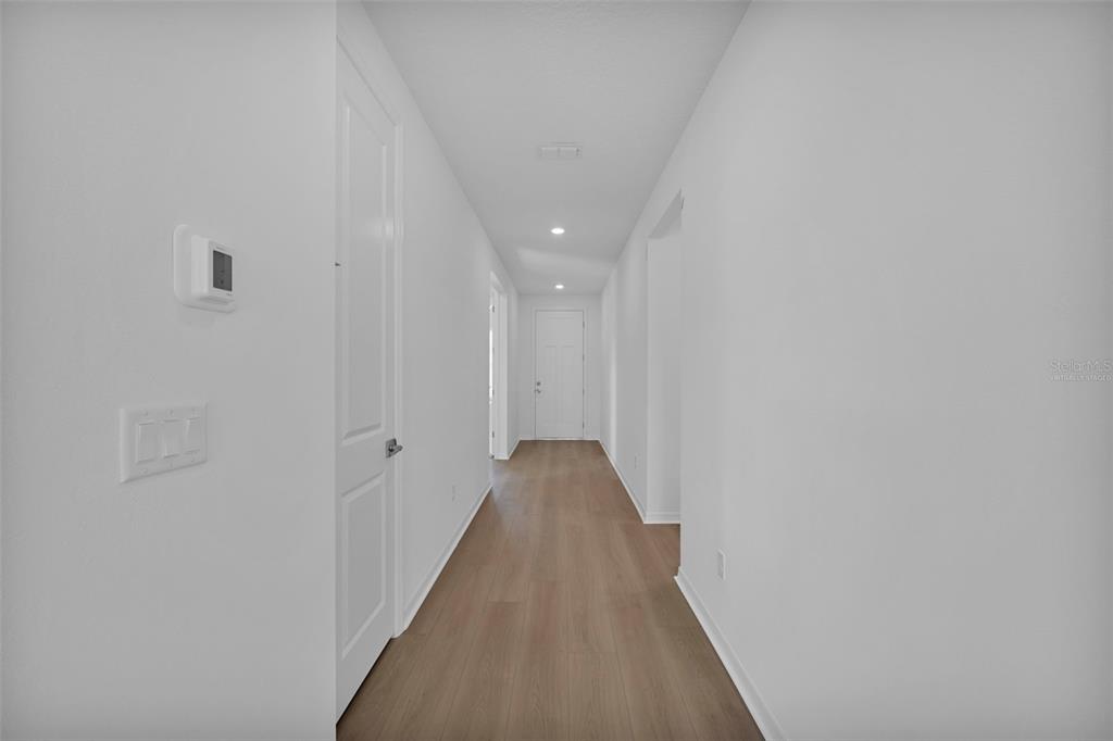 A long, narrow hallway with white walls, light wood-look flooring, and several closed white doors — 83 LAKE MANATEE DRIVE, PALM COAST, FL