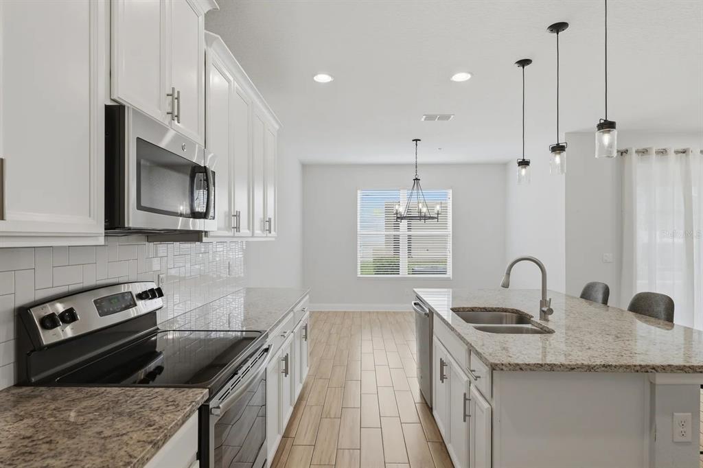 A modern kitchen features white cabinets, granite countertops, stainless steel appliances, and wood-look tile flooring — 15691 ORANGE HARVEST LOOP, WINTER GARDEN, FL