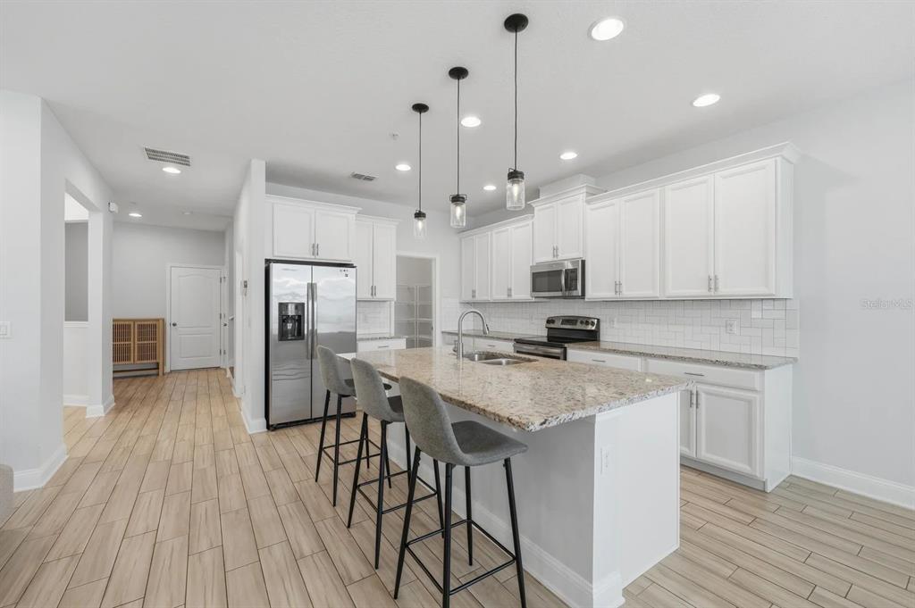 A modern kitchen features white cabinets, granite countertops, a center island, and wood-look tile flooring — 15691 ORANGE HARVEST LOOP, WINTER GARDEN, FL