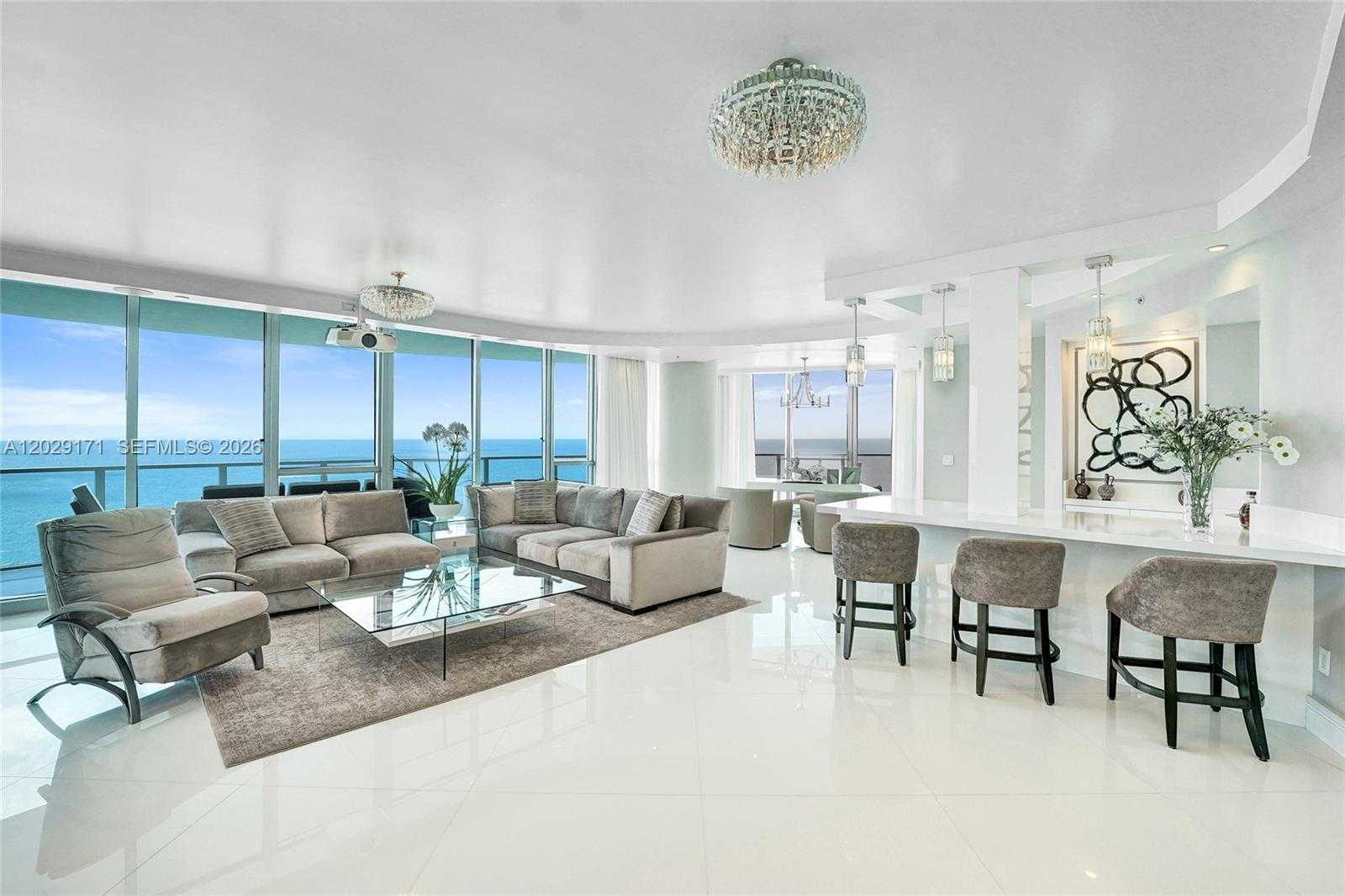 A modern living room and kitchen area features white tile floors, ocean views, and chandeliers — 3101 S Ocean Dr # 2208, Hollywood FL 33019, HOLLYWOOD, FL