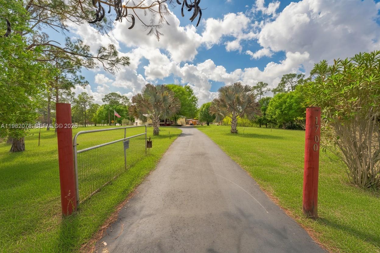 A paved driveway leads through a gated entrance toward a house surrounded by green lawns — 1700 Tampa Ave, Clewiston FL 33440, CLEWISTON, FL