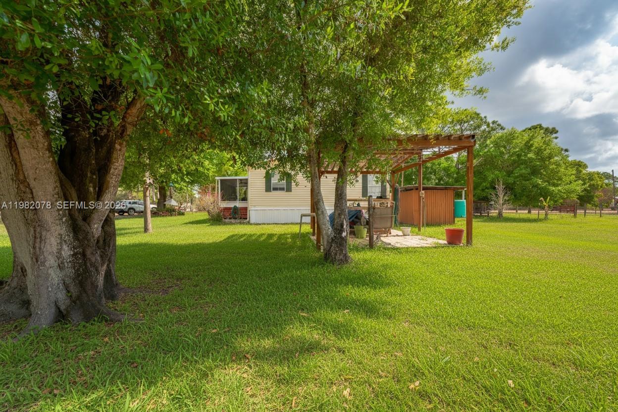 A grassy yard features a mobile home with a wooden pergola and mature trees — 1700 Tampa Ave, Clewiston FL 33440, CLEWISTON, FL