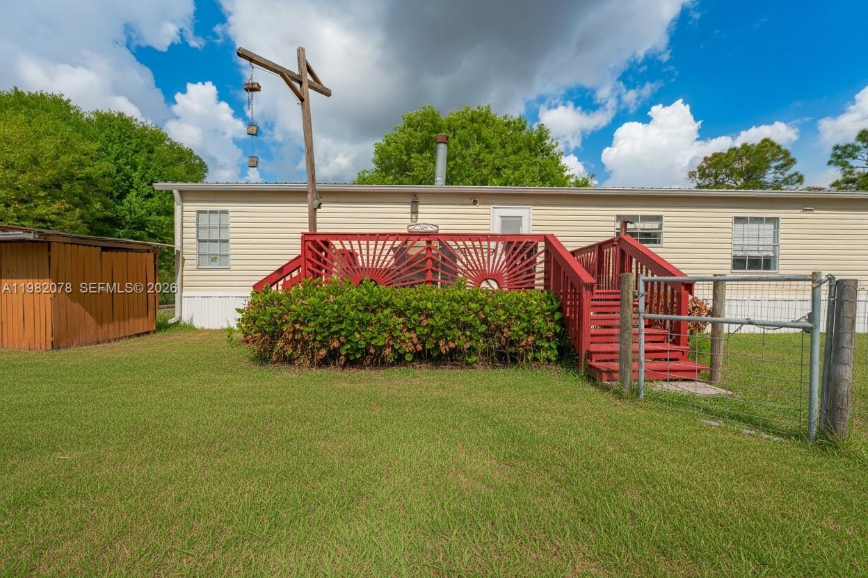 A tan mobile home features a red wooden deck and stairs in a grassy yard — 1700 Tampa Ave, Clewiston FL 33440, CLEWISTON, FL