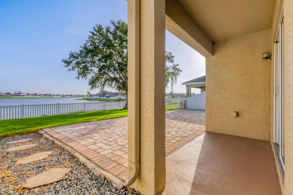 An empty living room with wood-look flooring, a pass-through window to the kitchen, and blinds — 31209 MASENA DRIVE, WESLEY CHAPEL, FL