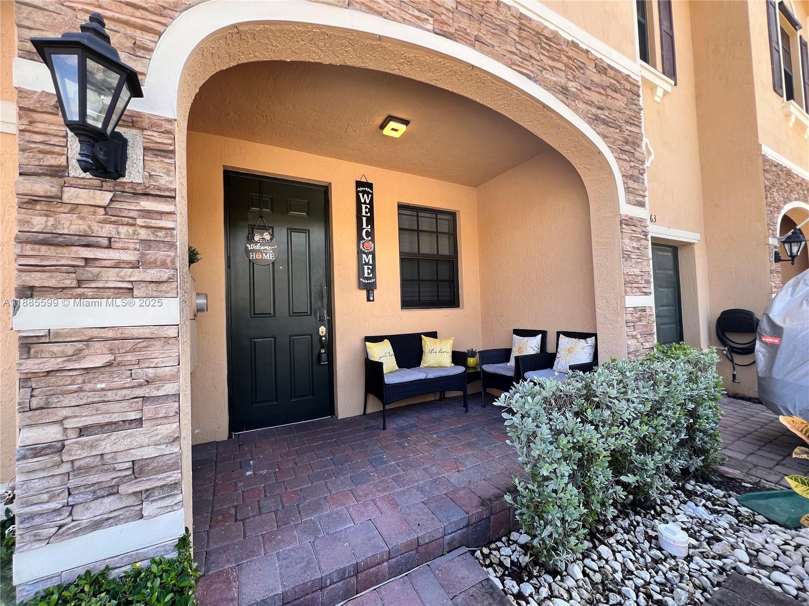 A covered front porch features a dark door, stone veneer accents, and patio furniture — 159 SE 34th Ave, Homestead FL 33033, HOMESTEAD, FL