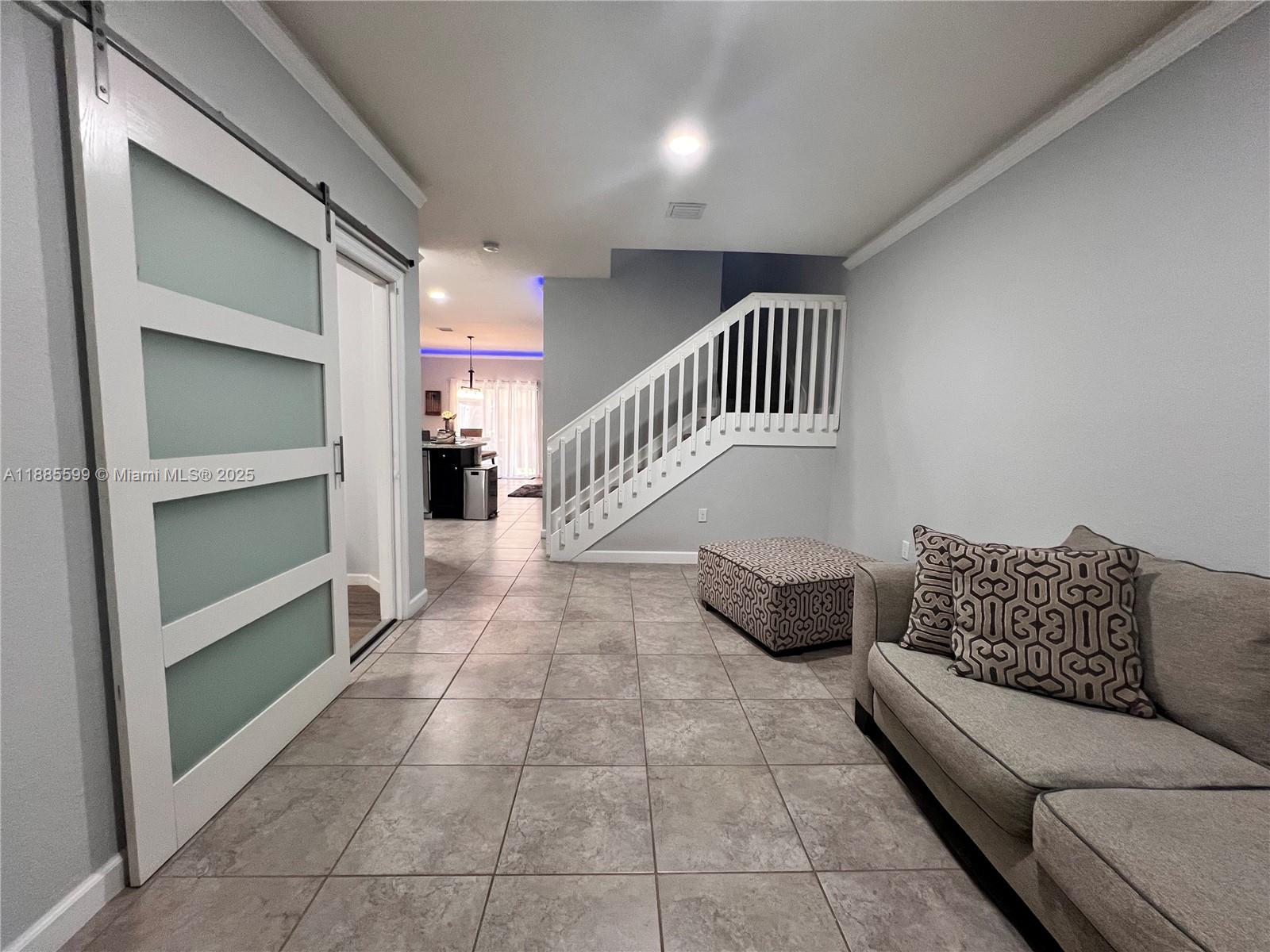 A living area features tile floors, a sliding barn door, and a staircase with railings — 159 SE 34th Ave, Homestead FL 33033, HOMESTEAD, FL