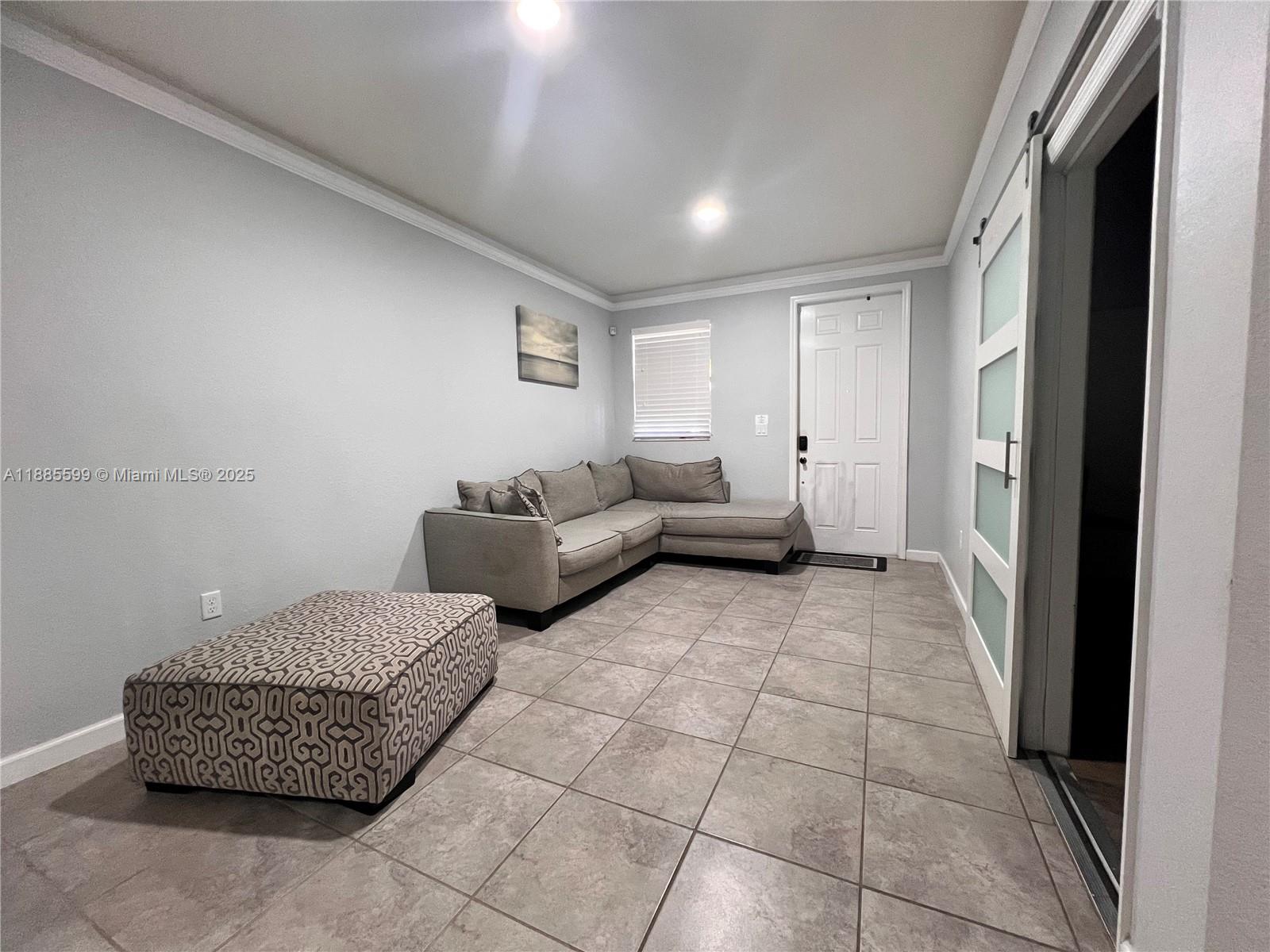 A living room features light gray walls, tile flooring, a sectional sofa, and an ottoman — 159 SE 34th Ave, Homestead FL 33033, HOMESTEAD, FL