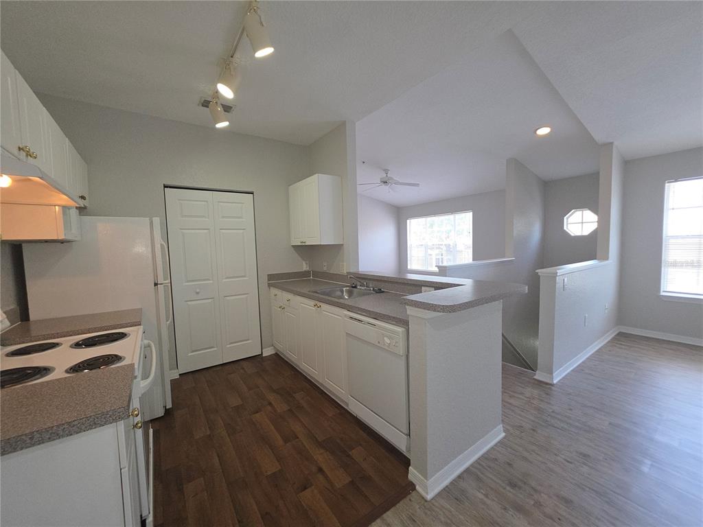 A kitchen with white cabinets, laminate countertops, and wood-look flooring overlooks a living area — 852 GRAND REGENCY POINT UNIT 202, ALTAMONTE SPRINGS, FL