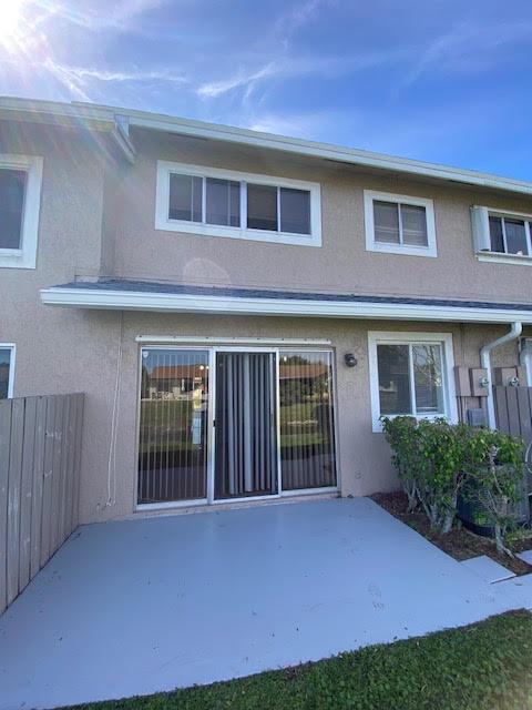 A beige two-story townhouse exterior features a concrete patio, sliding glass doors, and upper windows — 2217 Discovery Circle W, Deerfield Beach FL 33442, DEERFIELD BEACH, FL