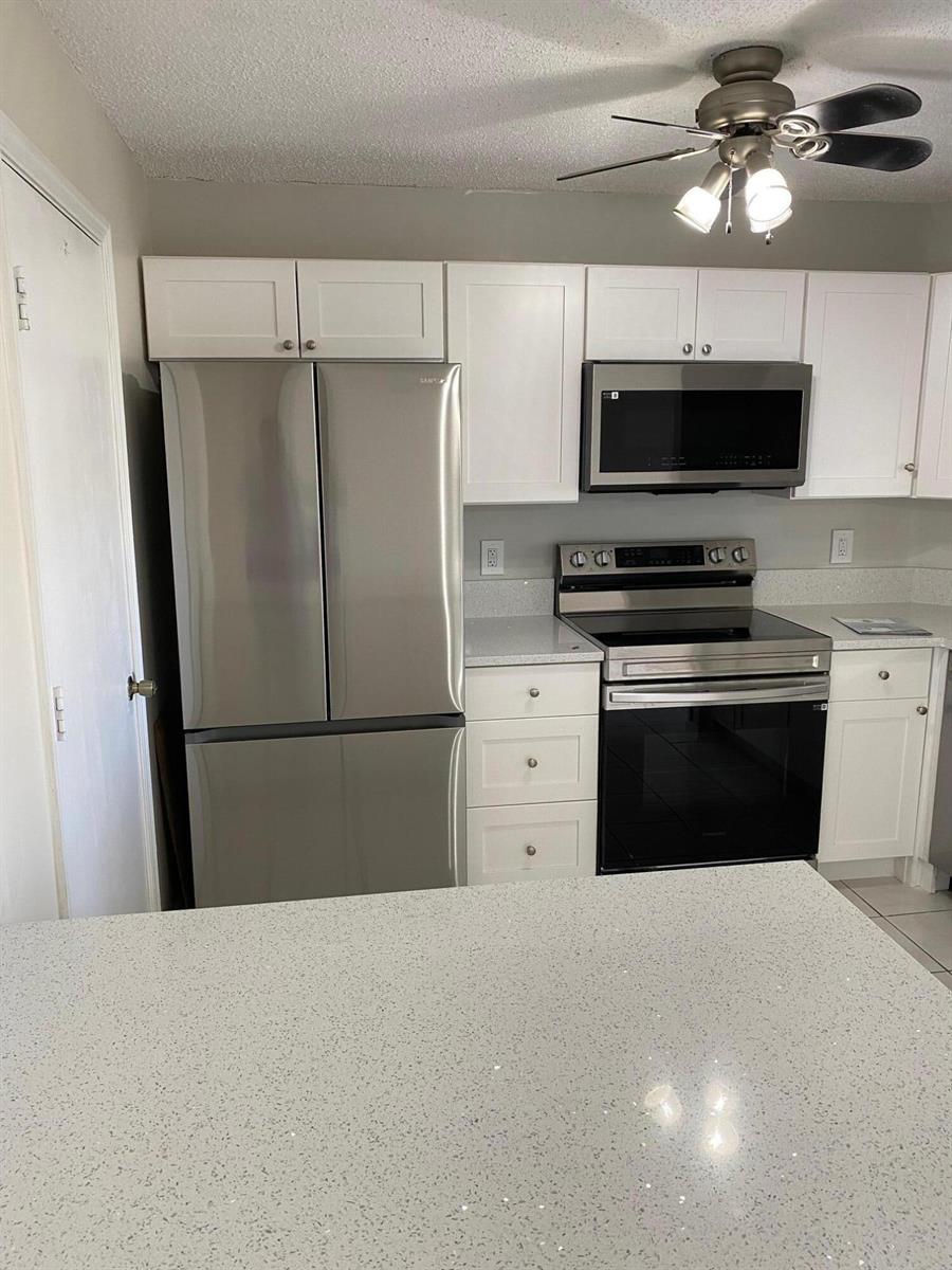 A kitchen features white cabinets, stainless steel appliances, and light-colored quartz countertops — 2217 Discovery Circle W, Deerfield Beach FL 33442, DEERFIELD BEACH, FL