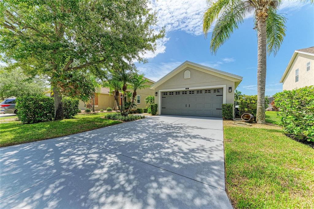 A single-story house with a gray garage door, a concrete driveway, and a palm tree — 14260 GNATCATCHER TERRACE, LAKEWOOD RANCH, FL