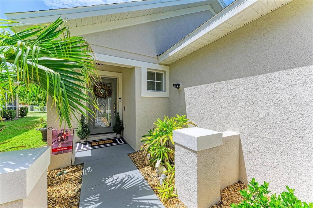 The exterior entrance of a house features a gray door, a walkway, and landscaping — 14260 GNATCATCHER TERRACE, LAKEWOOD RANCH, FL