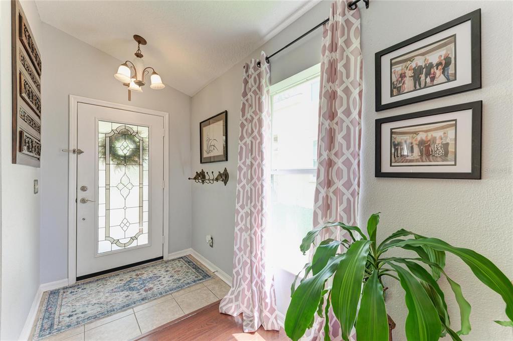 An entryway features a white front door, tile flooring, patterned curtains, and framed wall art — 14260 GNATCATCHER TERRACE, LAKEWOOD RANCH, FL