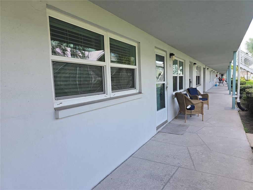 A concrete walkway runs along the exterior of a building with windows and patio chairs — 5267 81ST STREET N UNIT 5, ST PETERSBURG, FL