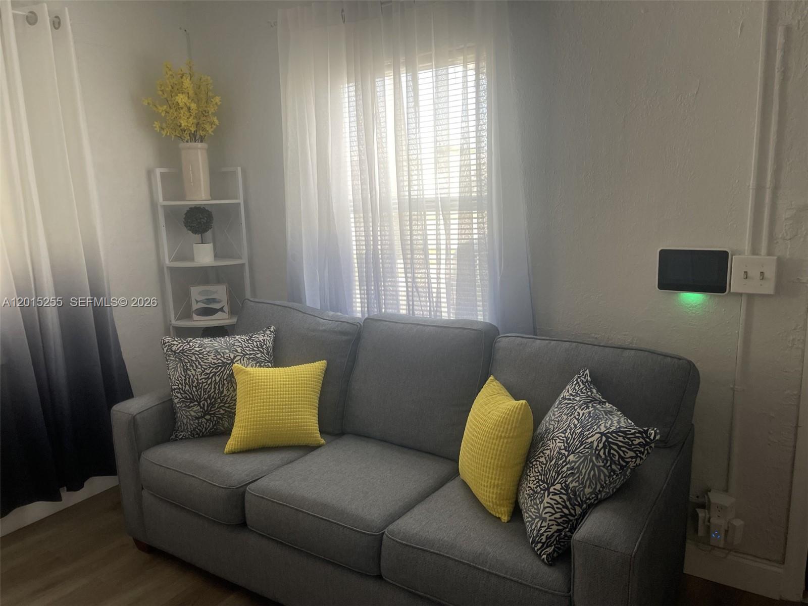 A gray sofa with yellow and patterned pillows sits in a room with white curtains — 1019 NW 4th Ave, Pompano Beach FL 33060, POMPANO BEACH, FL