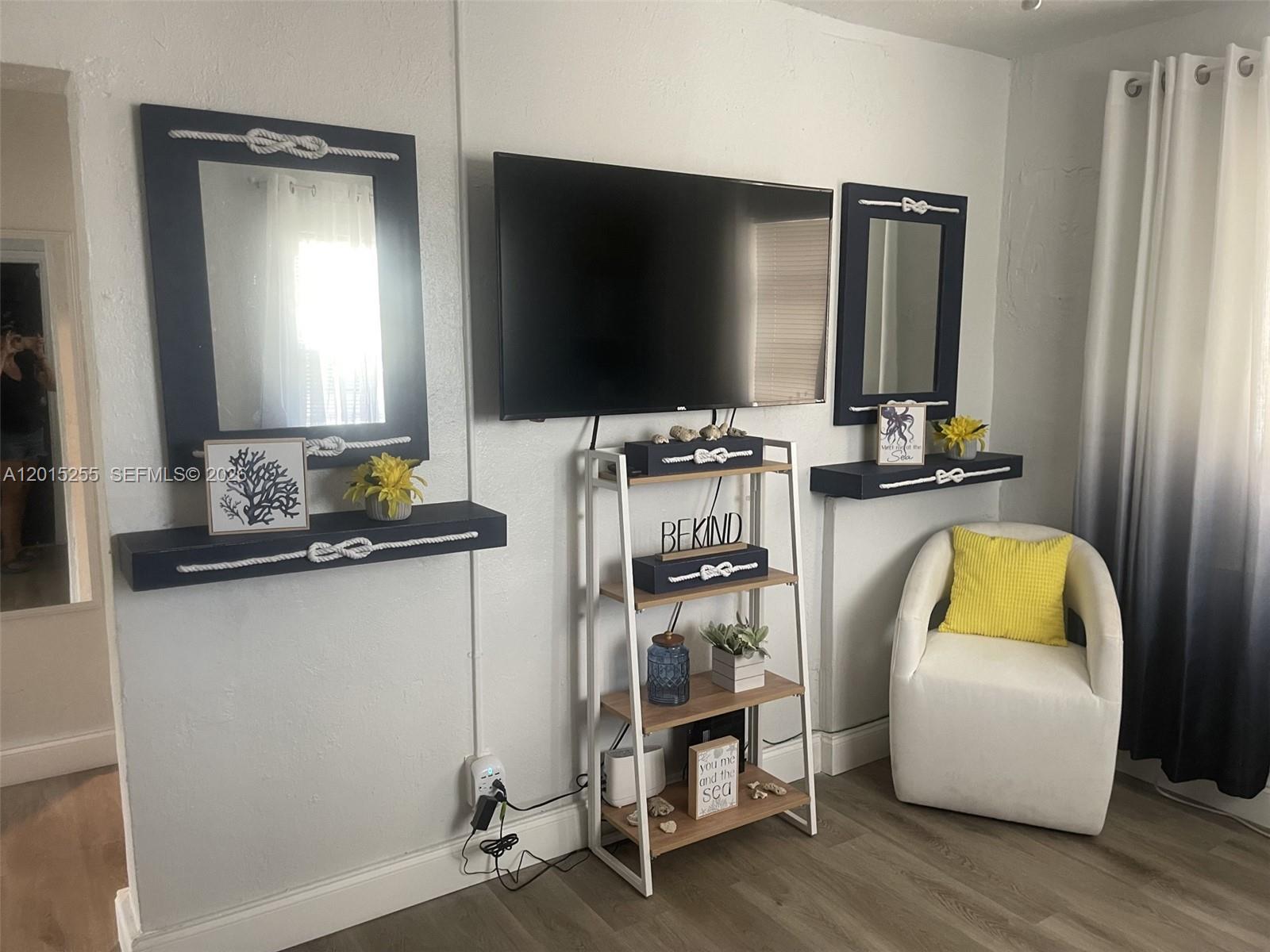 A living room features a wall-mounted television, two nautical-themed mirrors with shelves, and a chair — 1019 NW 4th Ave, Pompano Beach FL 33060, POMPANO BEACH, FL