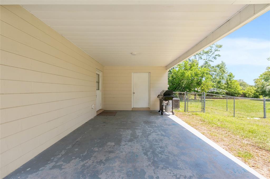 A covered concrete patio features light-colored siding, two white doors, and a backyard grill — 21545 SW HONEYSUCKLE STREET, DUNNELLON, FL