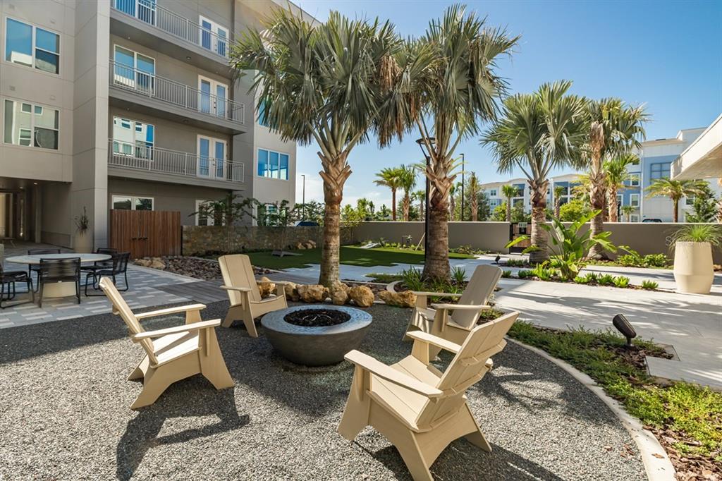 An outdoor patio area features a fire pit surrounded by chairs and palm trees — 11929 PIONEERS WAY UNIT C3.10, ORLANDO, FL